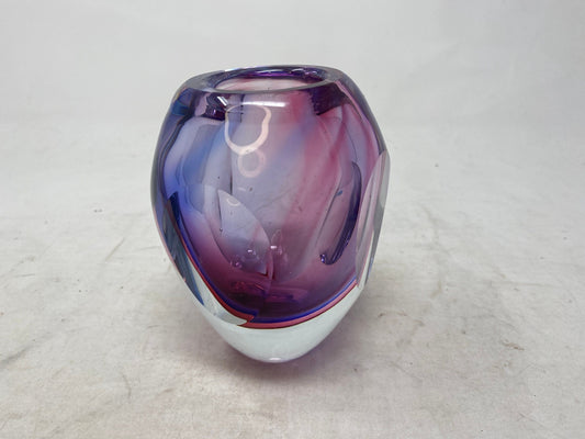 This vintage Murano vase, crafted using the iconic Sommerso technique, captivates with its mesmerizing blend of violet, raspberry blue, and sparkling clear glass. Standing at a petite 5 inches tall and 3.75 inches wide, this vase embodies mid-century elegance. Its graceful curves and compact form make it a versatile accent piece, perfect for displaying both bold blooms and delicate stems.